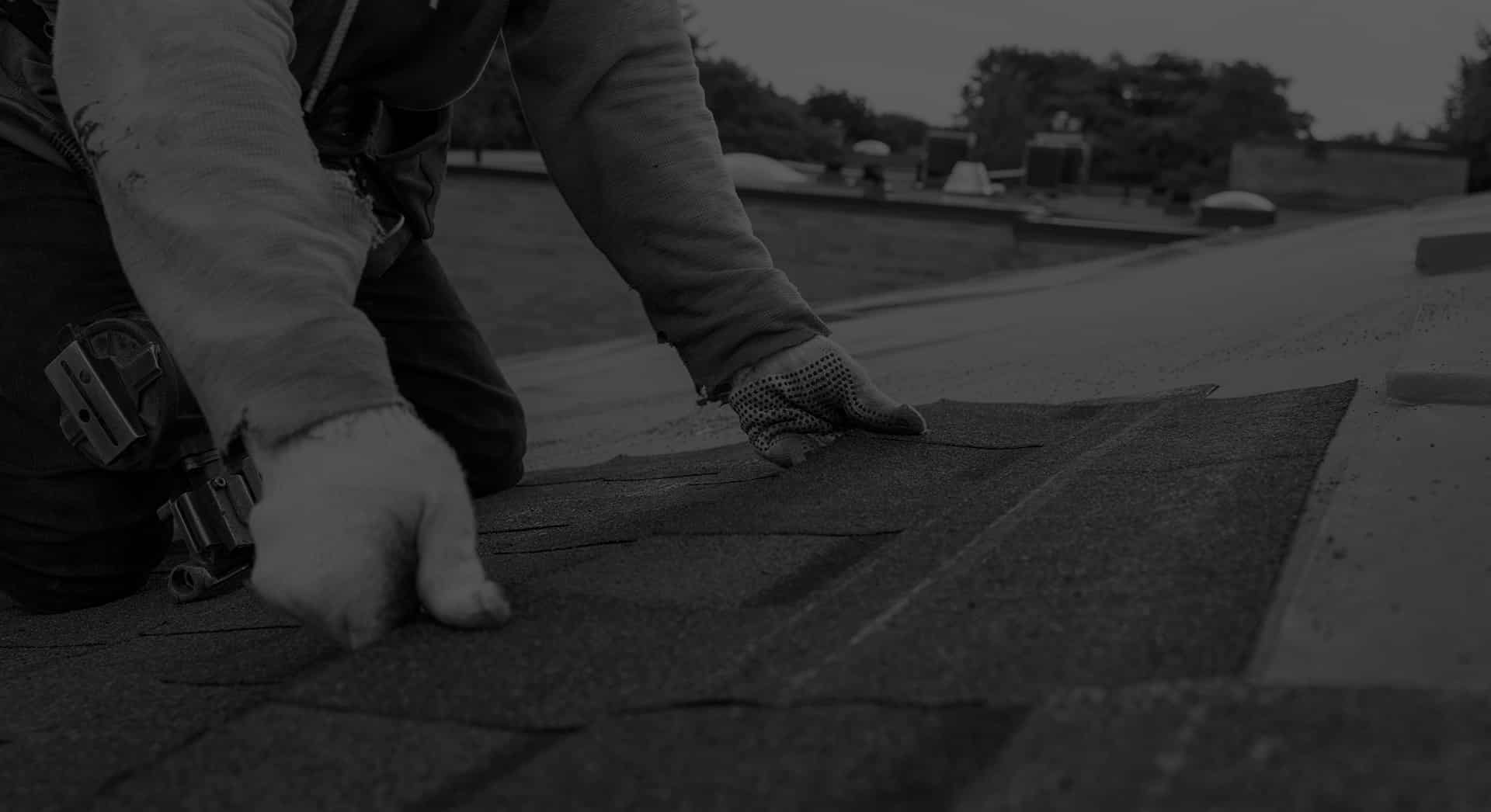 A person wearing gloves installs shingles on a rooftop, showcasing the precision and craftsmanship often seen with Dayton roofers.