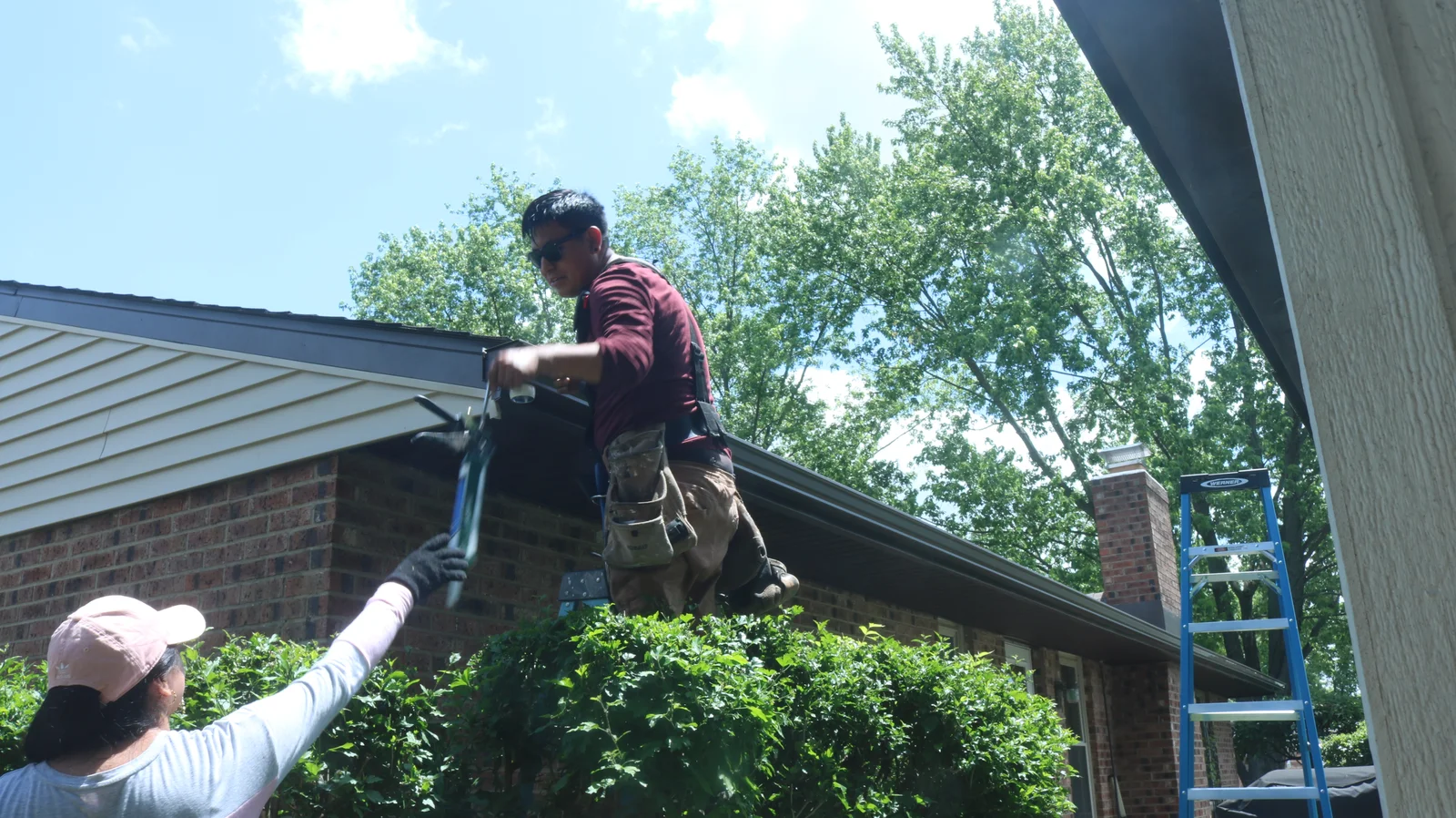 Two workers repairing gutters, one on a ladder and the other passing tools