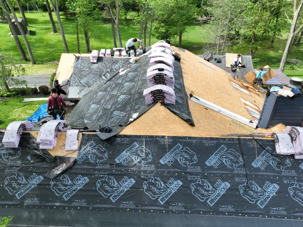 Aerial view of a house undergoing a roof replacement with workers and materials on the roof