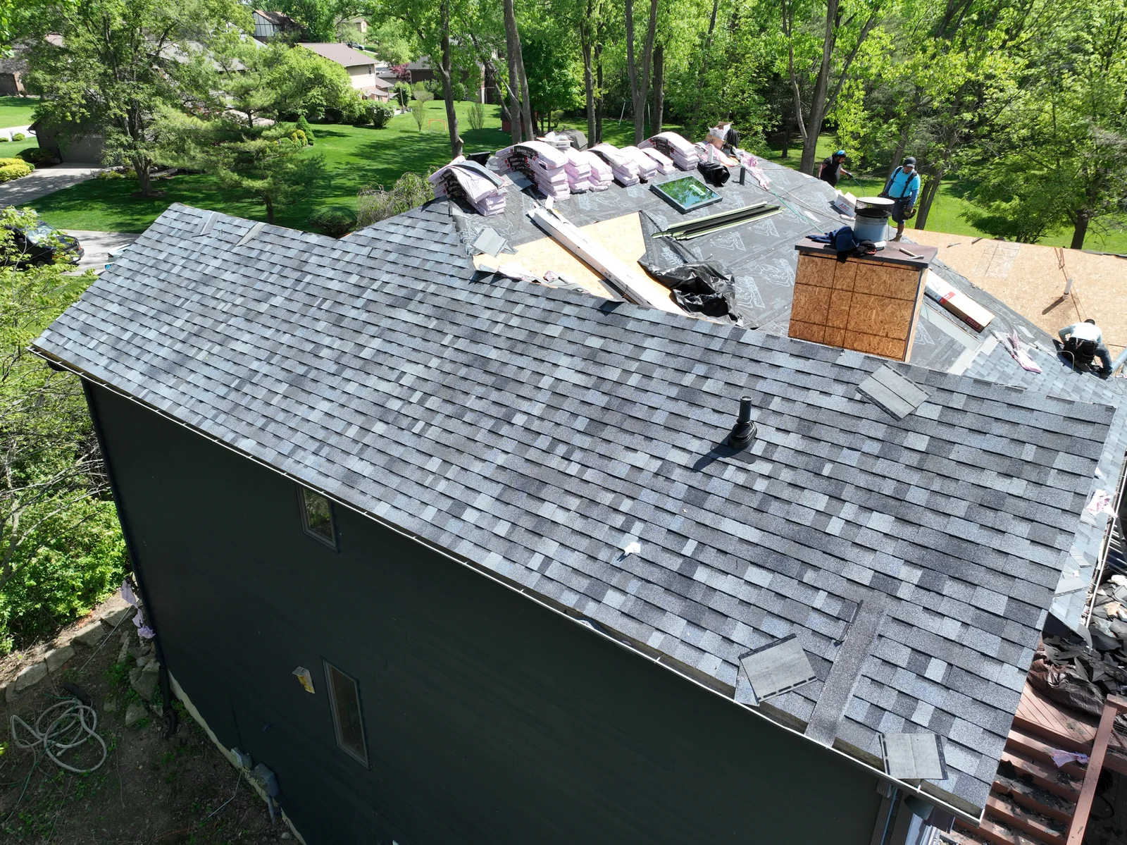 Aerial view of a house undergoing a roof replacement with workers and materials on the roof