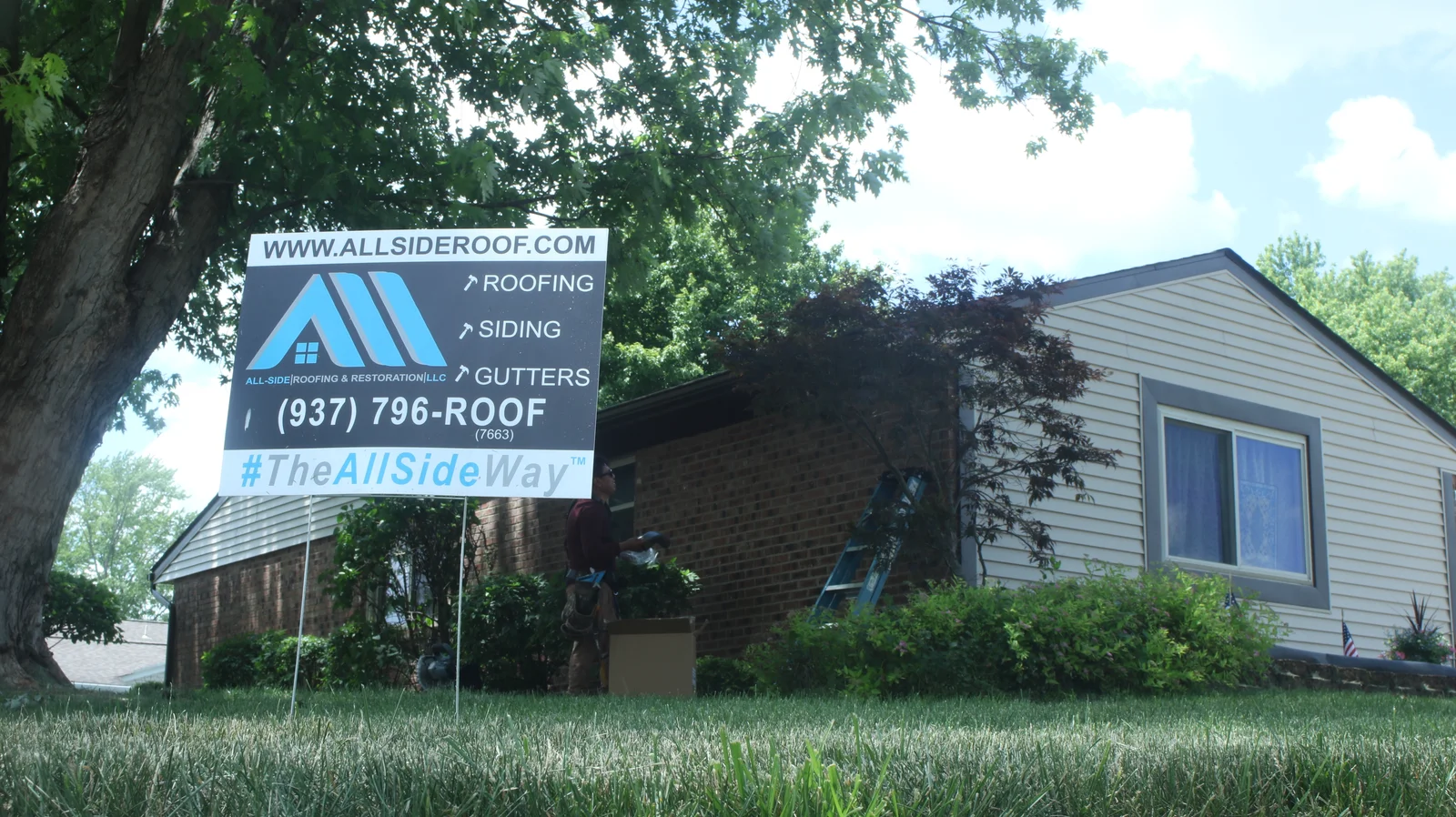 A sign for All-Side Roofing & Restoration LLC in front of a house, with a worker and a ladder visible in the background - Roof Types In Dayton