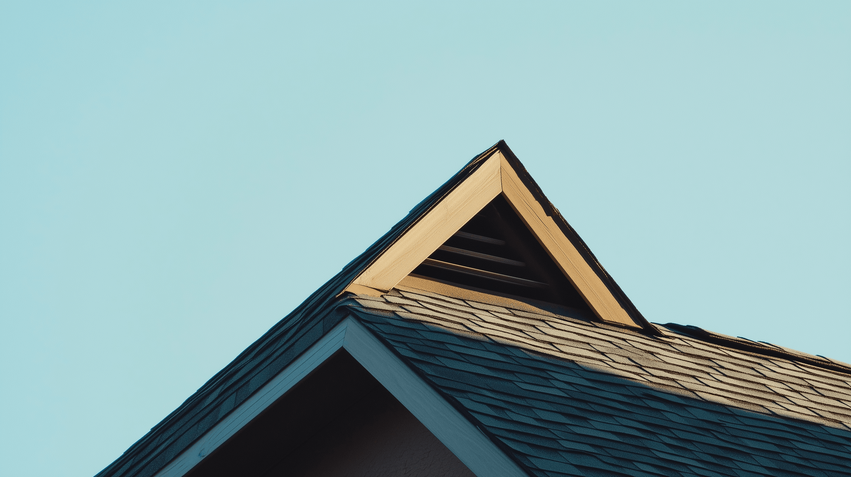A close-up view of a house roof with triangular eaves against a clear blue sky highlights the importance of proper ventilation for enhancing roof longevity.