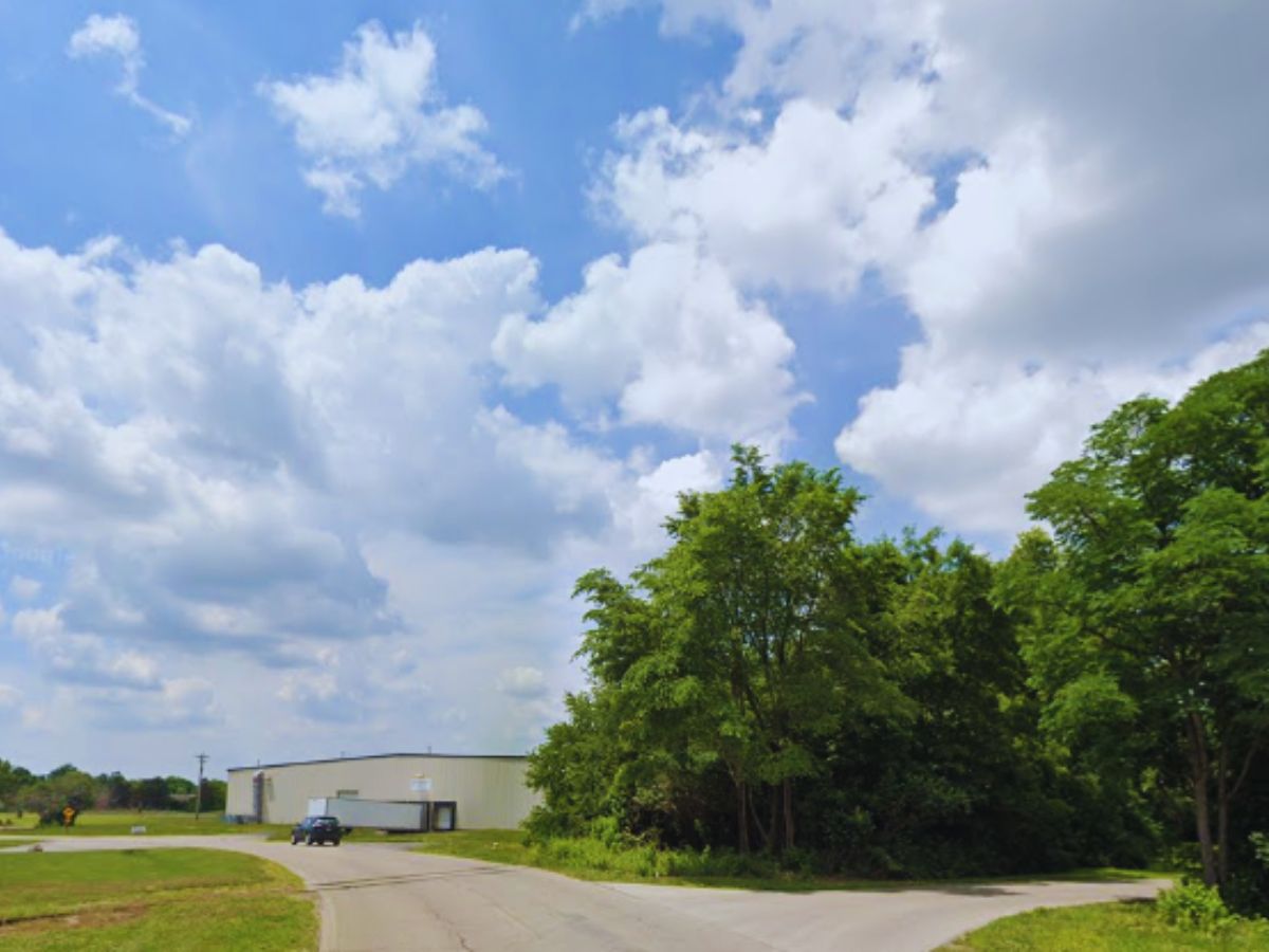 Warehouse building at 398 Industry Dr, Carlisle, with a large parking lot and a single vehicle, next to a green tree-lined road under partly cloudy OH skies.