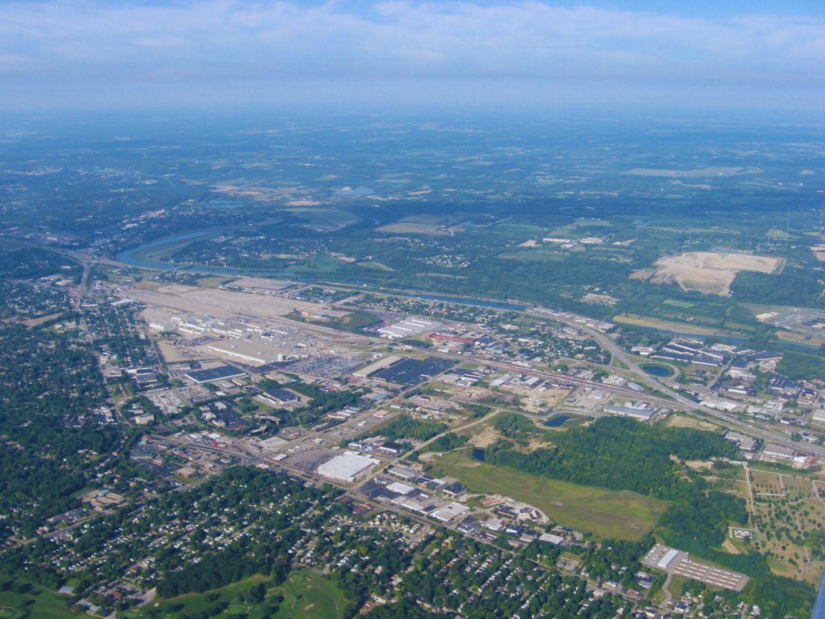 Aerial view of Moraine, OH, showcasing an industrial cityscape with a river winding through residential areas and greenery under a blue sky.