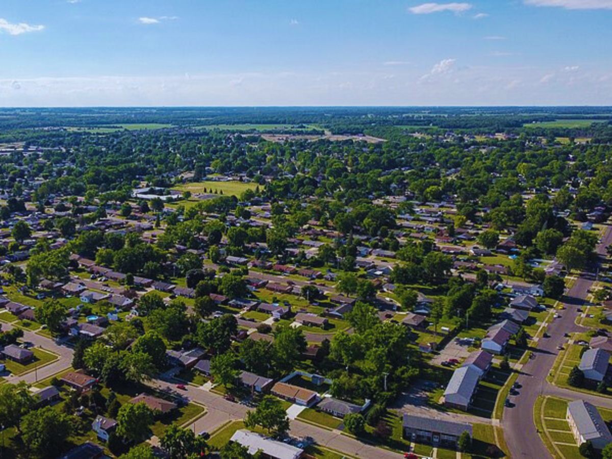Drone view of a suburban neighborhood in Troy, OH, showcasing houses, streets, and green trees on a sunny day.