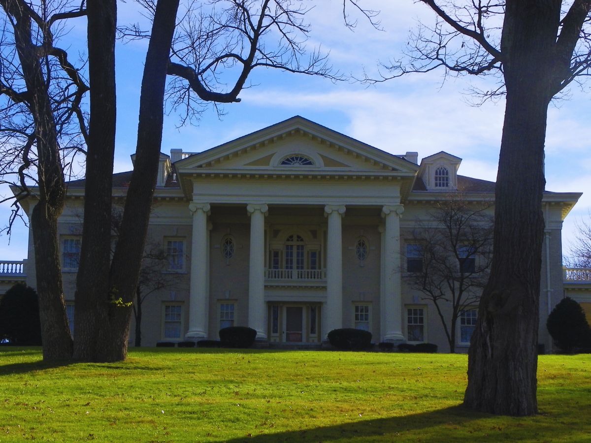 A large, two-story neoclassical building with grand columns and triangular pediment in Oakwood, set against a clear blue sky, framed by bare trees.
