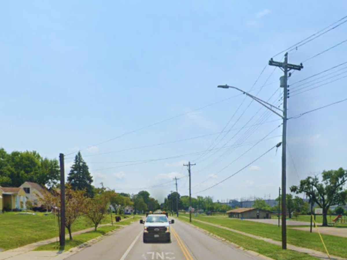 A car drives down Highland St in Middletown, flanked by grassy lawns and power lines under a clear blue sky.