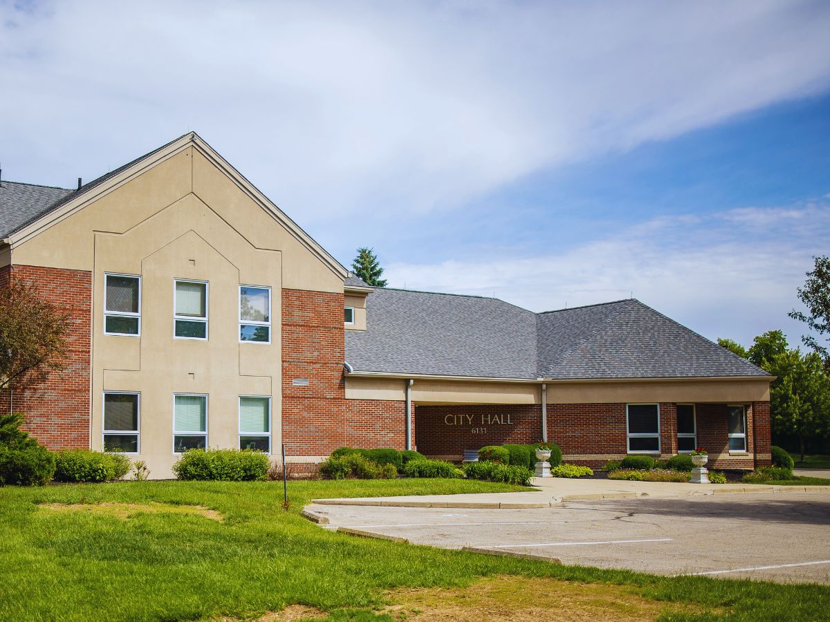Huber Heights City Hall features brick and beige walls, nestled amid lush greenery under a clear OH sky.