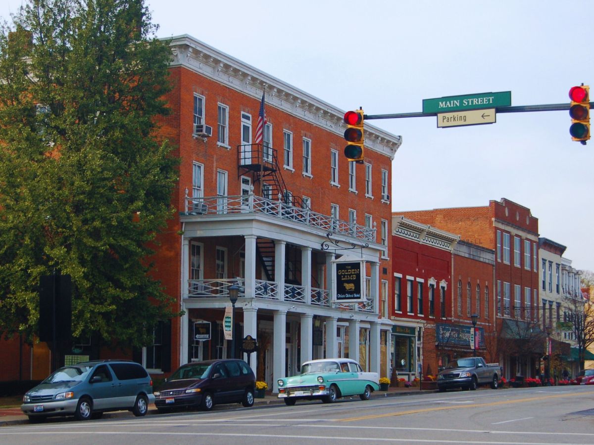 Historic brick buildings line a street with parked cars and a traffic light at an intersection under a Main Street sign in Lebanon, OH.