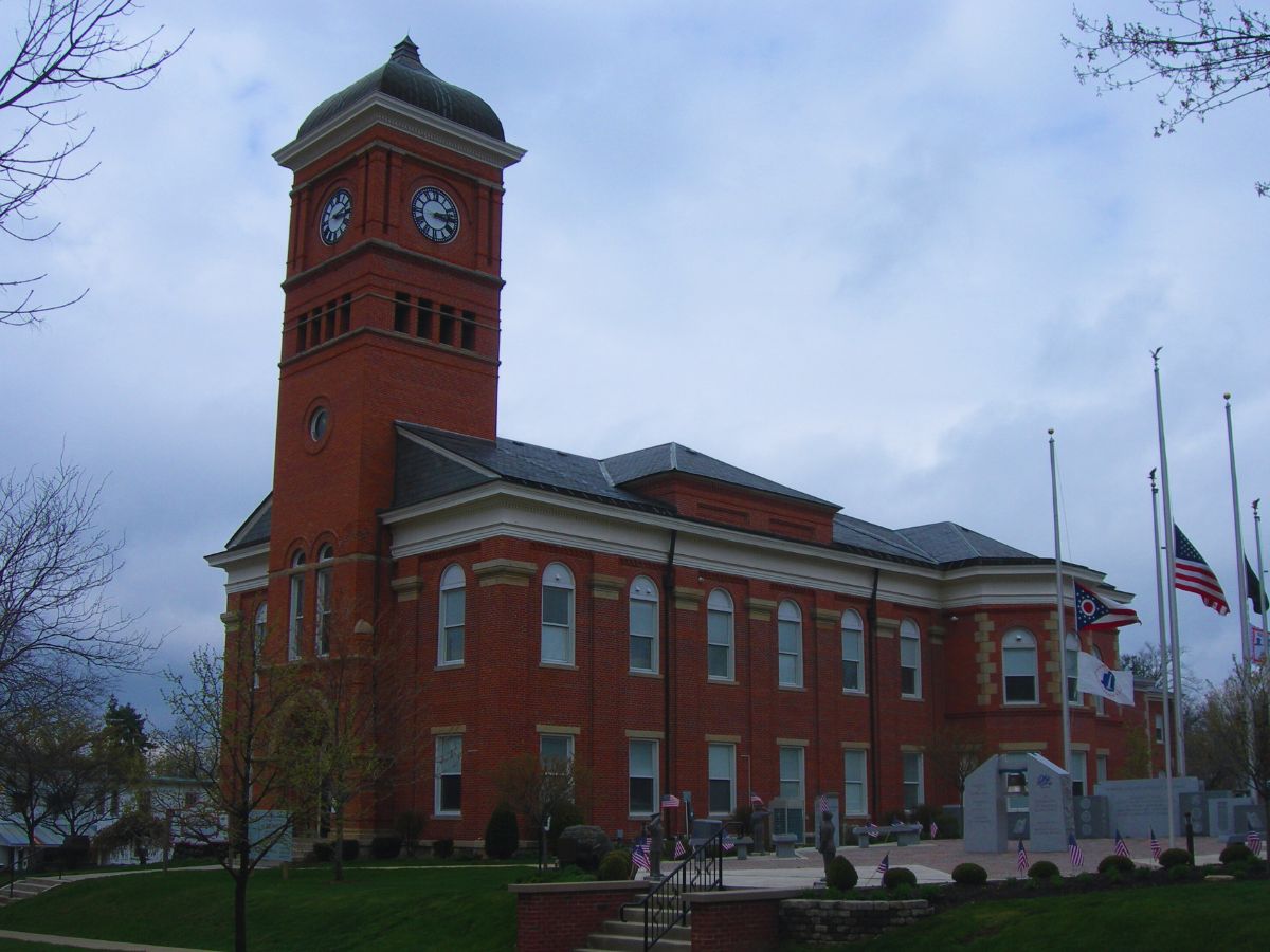 Historic red brick Morrow County Courthouse with clock tower, surrounded by flags and trees, under a cloudy OH sky.