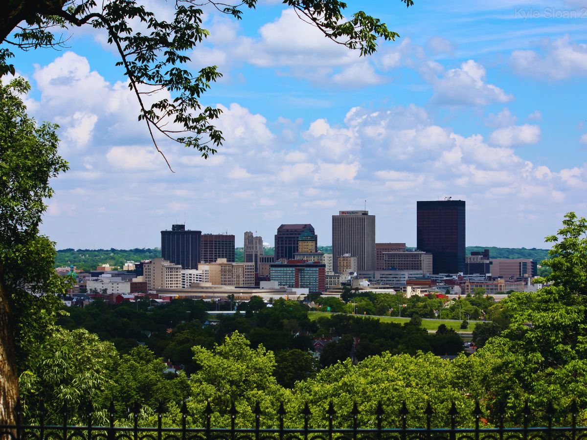 Dayton skyline with tall buildings and a lush, natural view of trees under a partly cloudy sky.