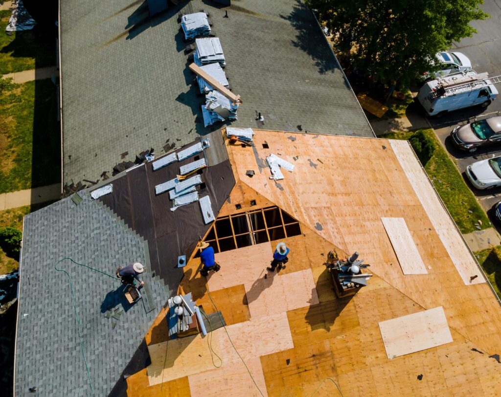Arial view of a roofing crew from a top-rated Greene County company working on a residential roof, plywood exposed, tools ready, shingles partially installed.