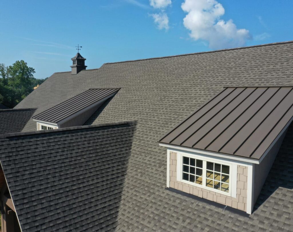 A roof with gray shingles, typical of Kettering, OH, boasts two dormer windows under a blue sky with scattered white clouds.