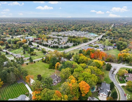Aerial view of a Greene County, OH suburban neighborhood with houses, roads, and colorful autumn trees under a partly cloudy sky.