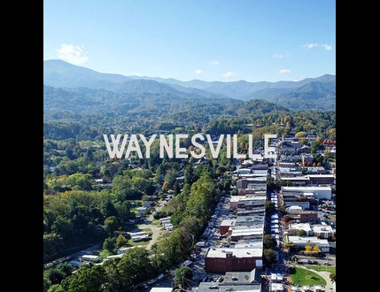 Aerial view of Waynesville, Ohio, with buildings below and forested mountains in the background under a clear blue sky.