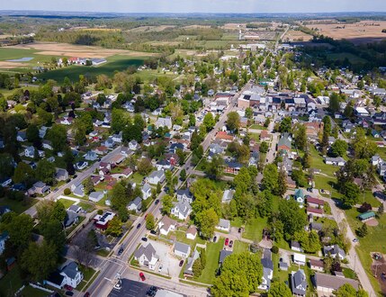 Aerial view of a small town in Champaign County, Ohio, with houses, trees, roads, and fields visible on a clear day.