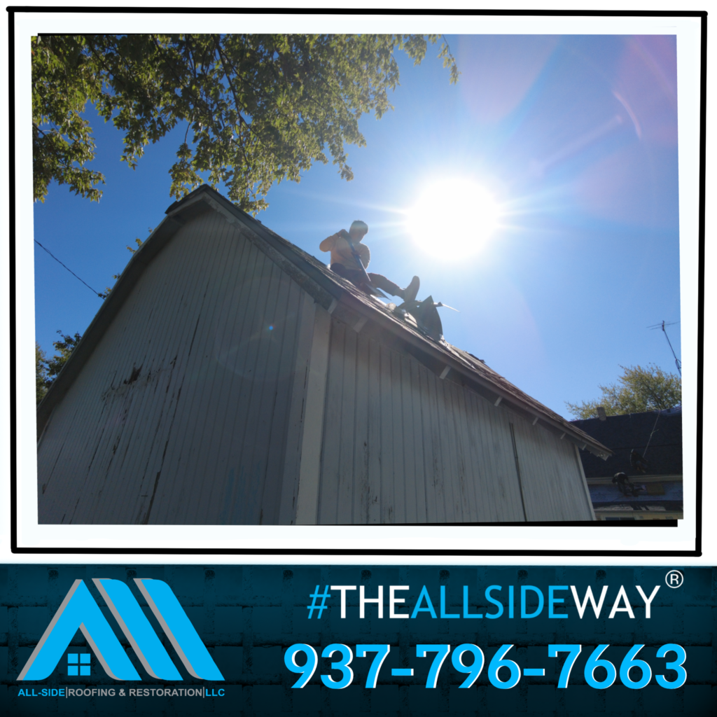 Person on a rooftop in bright sunlight, working on roof repairs; Roof Replacement experts in Dayton OH. Company logo and phone number shown below.