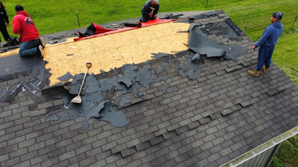 Three workers in Franklin OH perform roof replacement, removing old shingles and materials to reveal the plywood sheathing underneath.