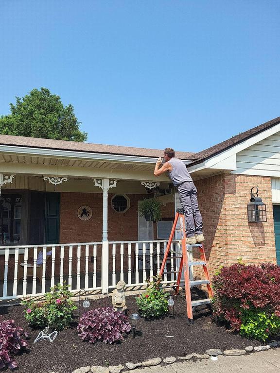 Person stands on ladder inspecting or working near the roof edge of a brick house, possibly for a roof replacement in Carlisle OH.