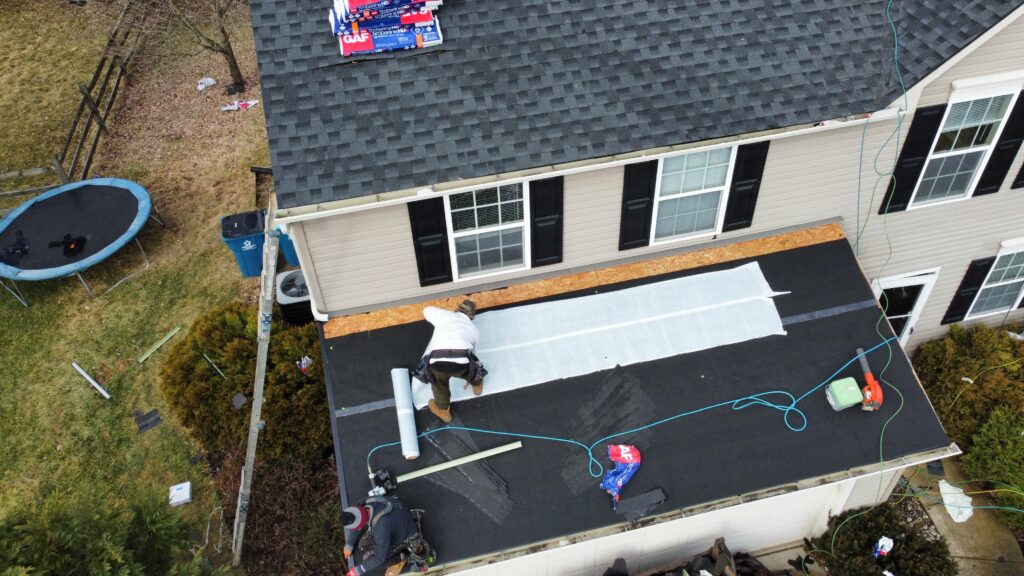 Two workers in Morrow, OH, install roofing material on a house extension as tools and supplies are scattered about during the roof replacement.