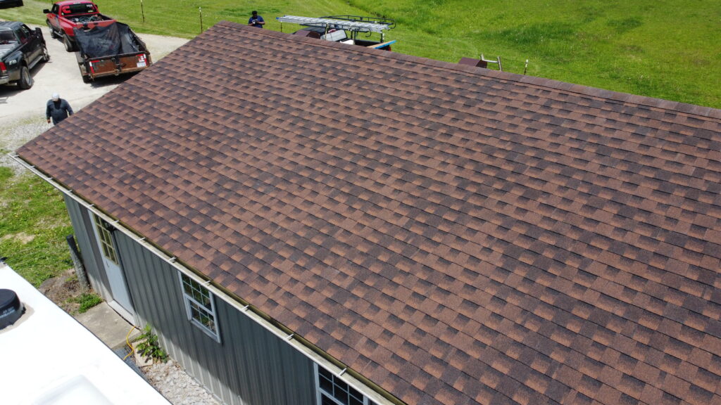 Aerial view of a brown shingle roof after roof replacement on a gray building in Franklin OH, near grass and vehicles in the driveway.