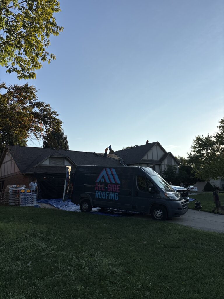 A dark gray All-Side Roofing van in a driveway while crew members perform a roof replacement in Kings Mills, OH.