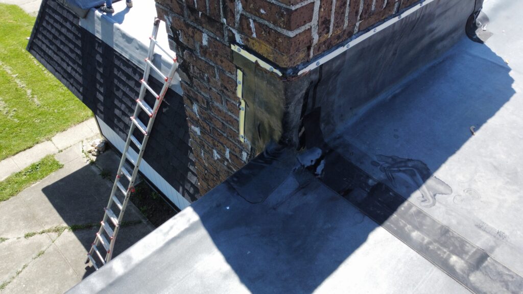 A brick chimney with rubber roofing flashing and an extension ladder on a roof replacement project in Maineville, OH.