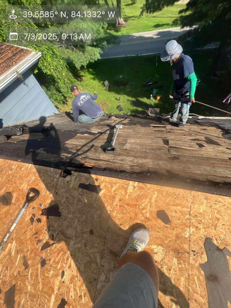 Two workers performing a roof replacement by removing old shingles from a residential house in Waynesville, OH.
