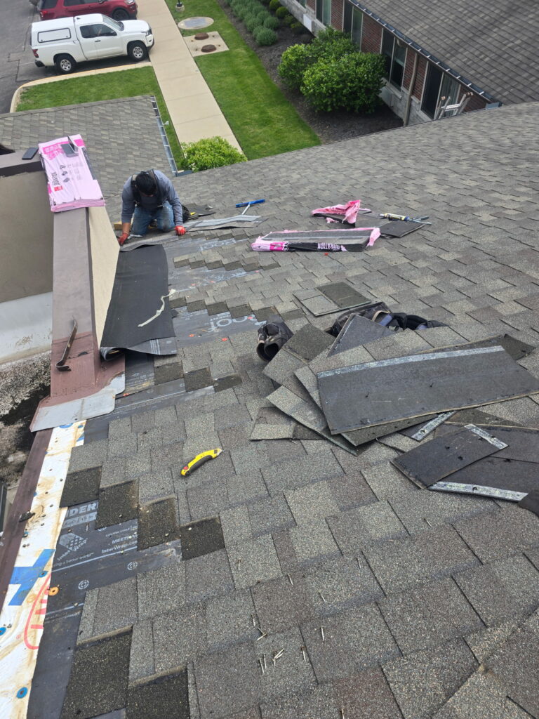 A worker in work clothes kneels on a residential roof in Wilmington, OH, installing shingles and roofing materials.