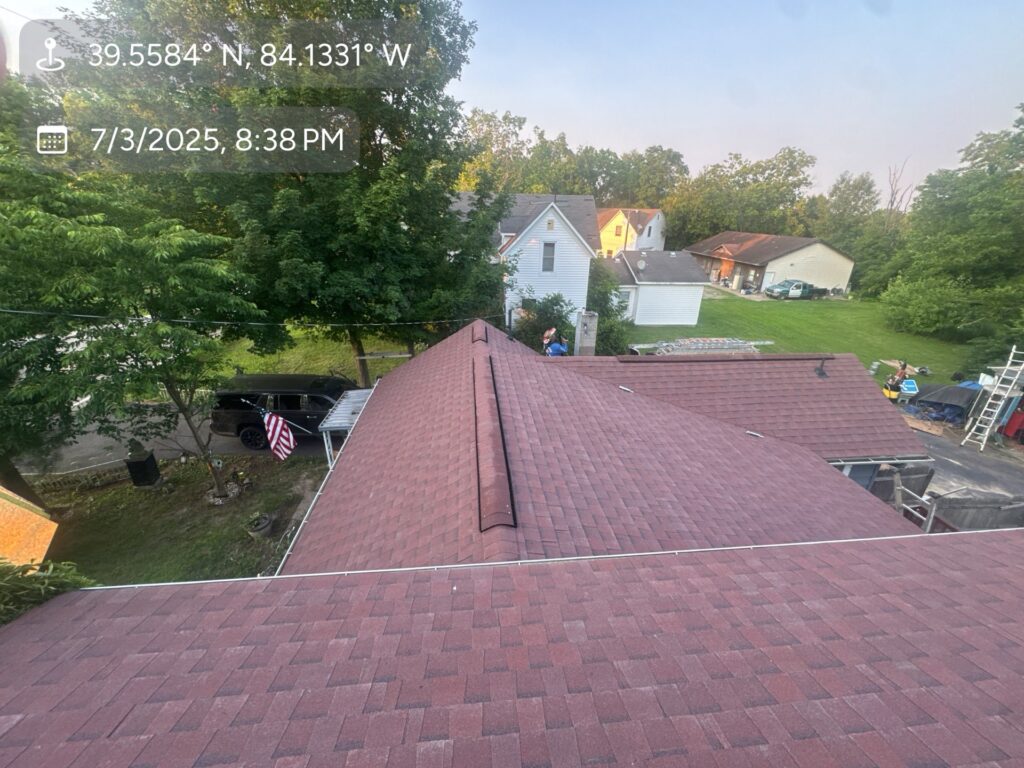 Elevated view of a shingled roof after a roof replacement in Waynesville, OH, overlooking a suburban backyard with a parked car and American flag.